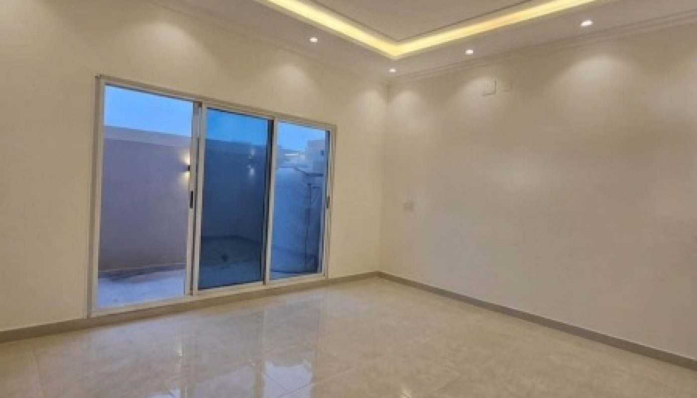 Empty room with glossy tiled floor, recessed ceiling lights, and large sliding glass doors opening to an outdoor area. Walls and ceiling are painted white.