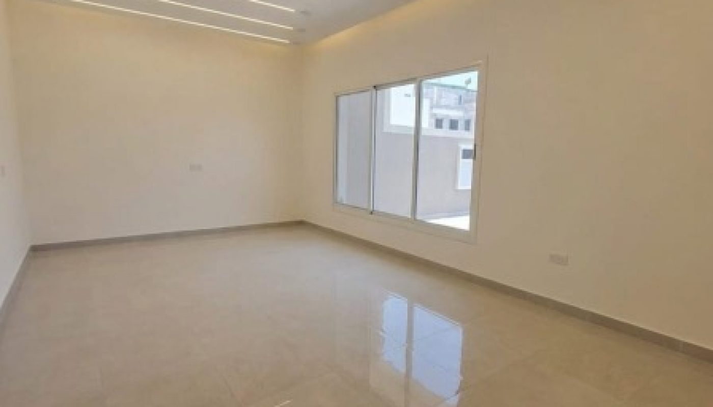 Empty modern room with large floor tiles, white walls, ceiling LED strip lights, and sliding glass doors that open to an outdoor area.