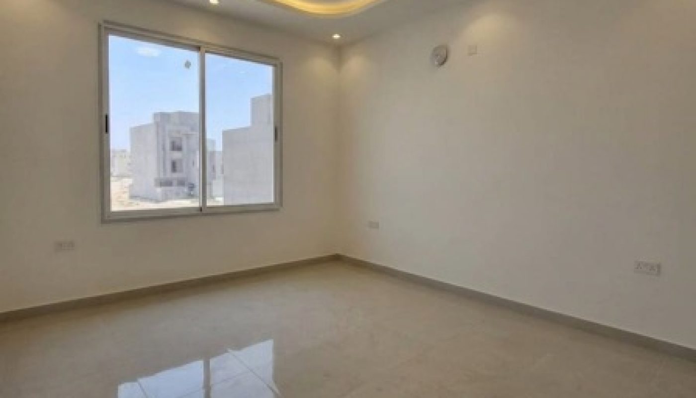 Empty room with beige tiled floor, white walls, a large window, and recessed ceiling lights with cove lighting. Natural daylight enters through the window, reflecting on the floor.