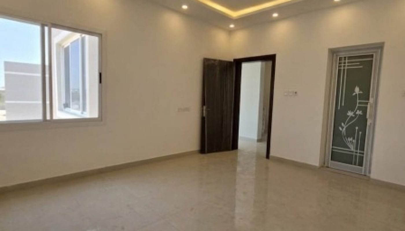 Empty, modern room with glossy tiled floors, recessed ceiling lights, a window, a dark wooden door, and a glass door with decorative frosted patterns.