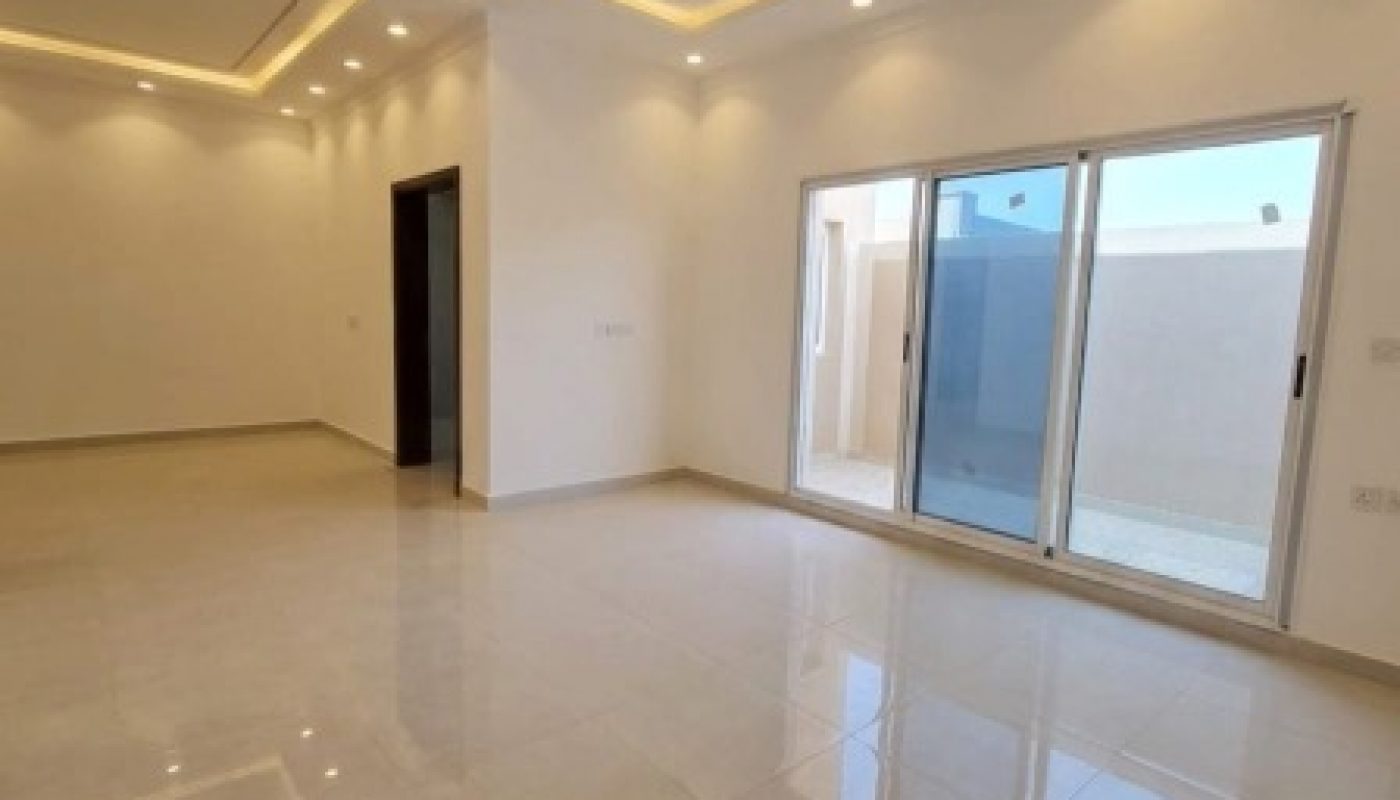 Spacious empty room with white walls, glossy tiled floor, recessed ceiling lights, and large sliding glass doors leading to an outdoor area.