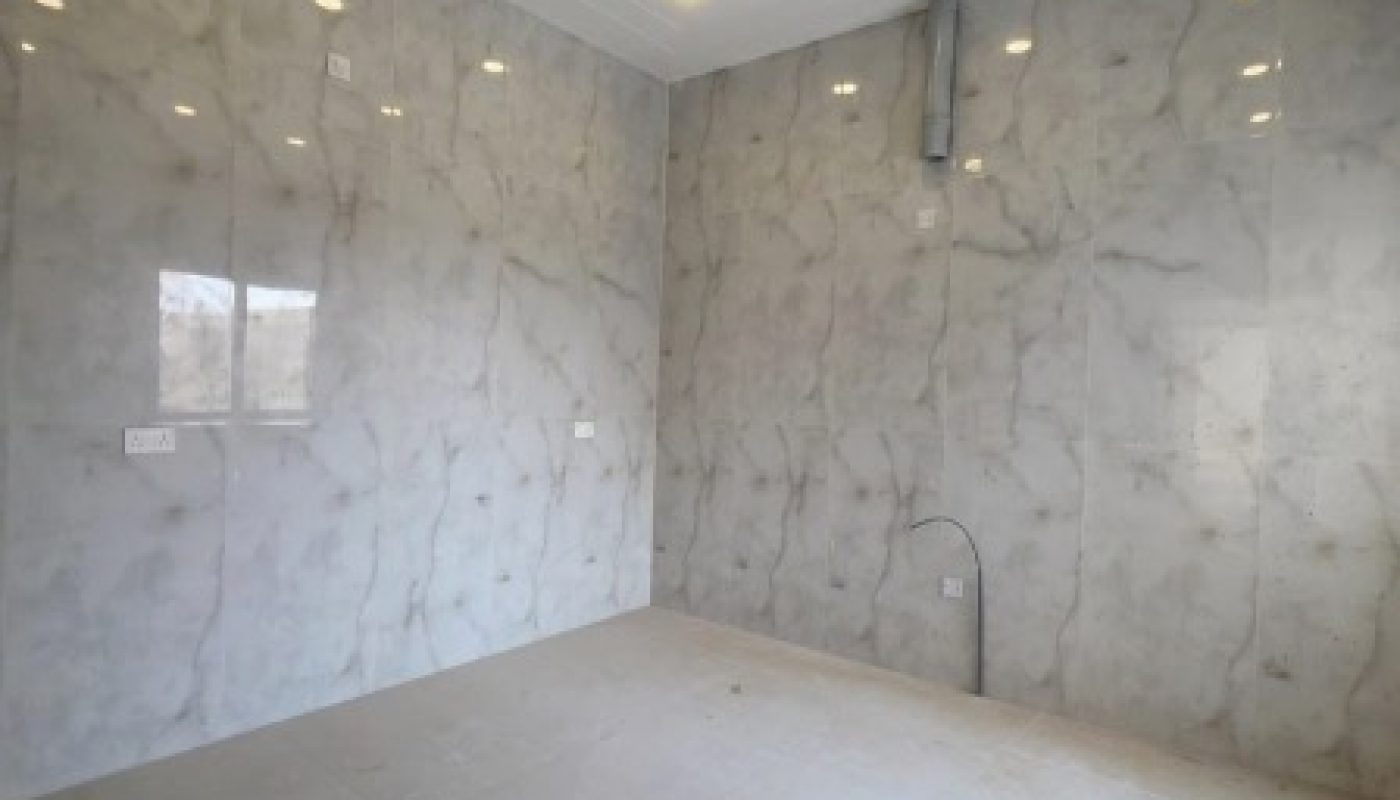Empty room with glossy marble-patterned walls and floor, ceiling lights, electrical outlets, and exposed pipe on the back wall.