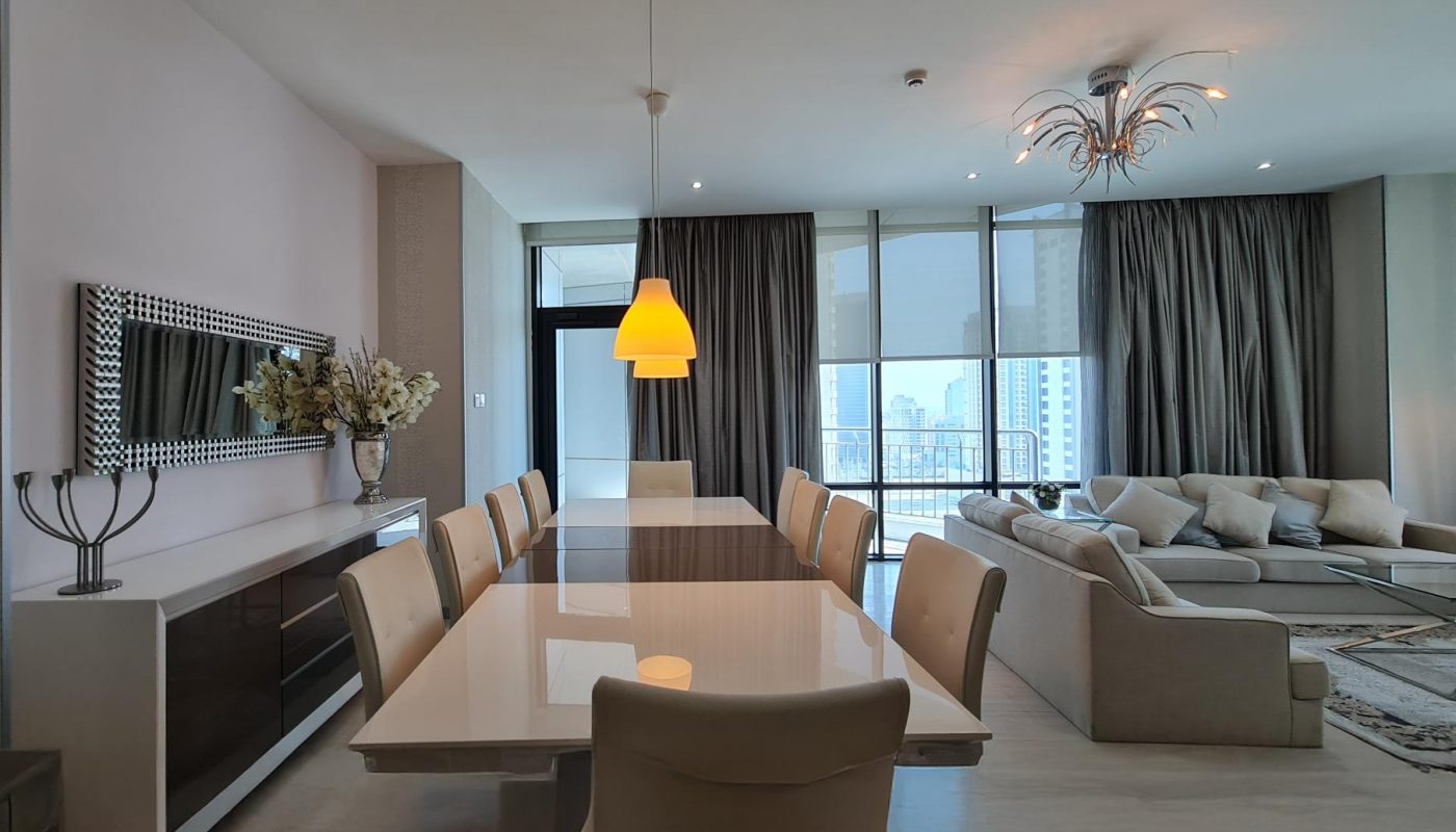 Modern living and dining area with a glossy dining table, beige chairs, pendant light, large windows with city view, and neutral-toned sofas.