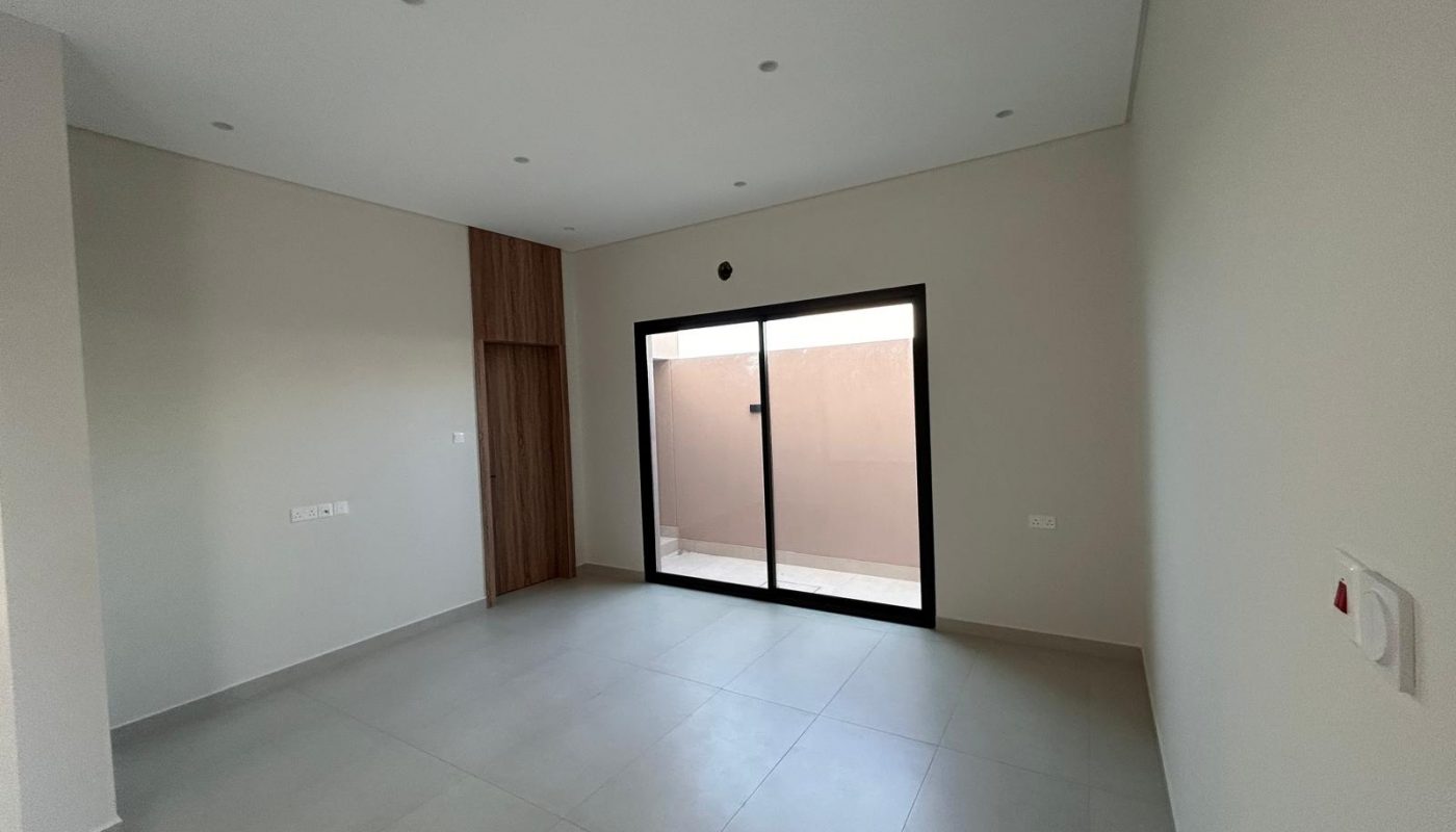 Empty room with light gray tile flooring, off-white walls, built-in wooden storage, and a large glass sliding door leading to an outdoor area.