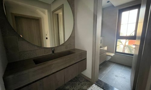 A huge bathroom in a luxury villa on Dilmunia Island, featuring a round mirror and tiled floor.