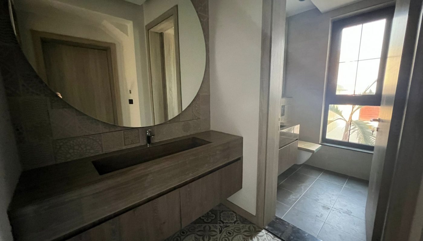 A huge bathroom in a luxury villa on Dilmunia Island, featuring a round mirror and tiled floor.