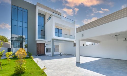 A modern house with a garage and a driveway, featuring a pool and bright garden.