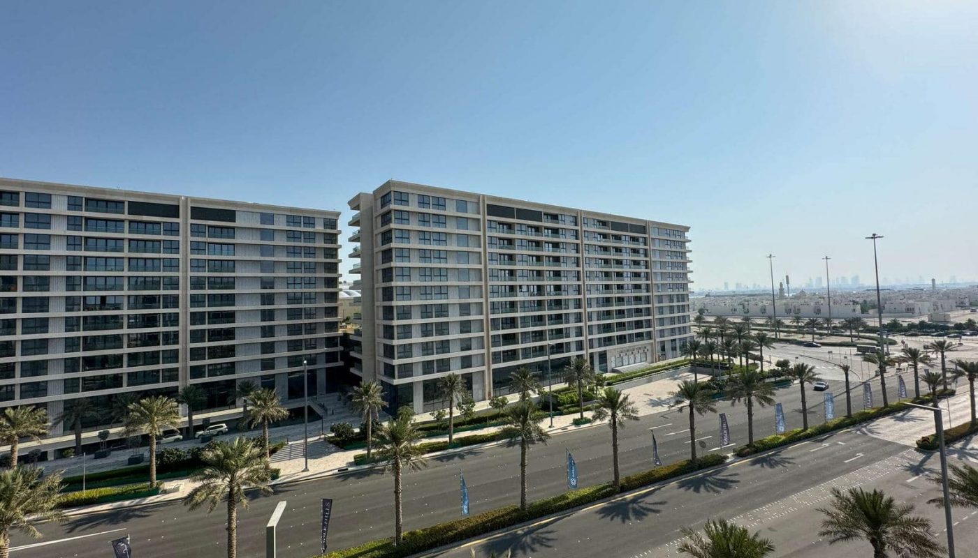 Aerial view of luxurious apartment buildings lining a palm tree-lined street under a clear blue sky.