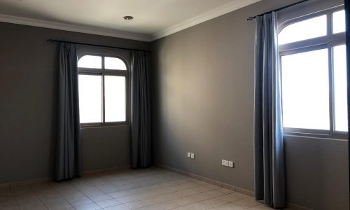 Empty room with gray walls, tile flooring, two windows with gray curtains, and ceiling lights.