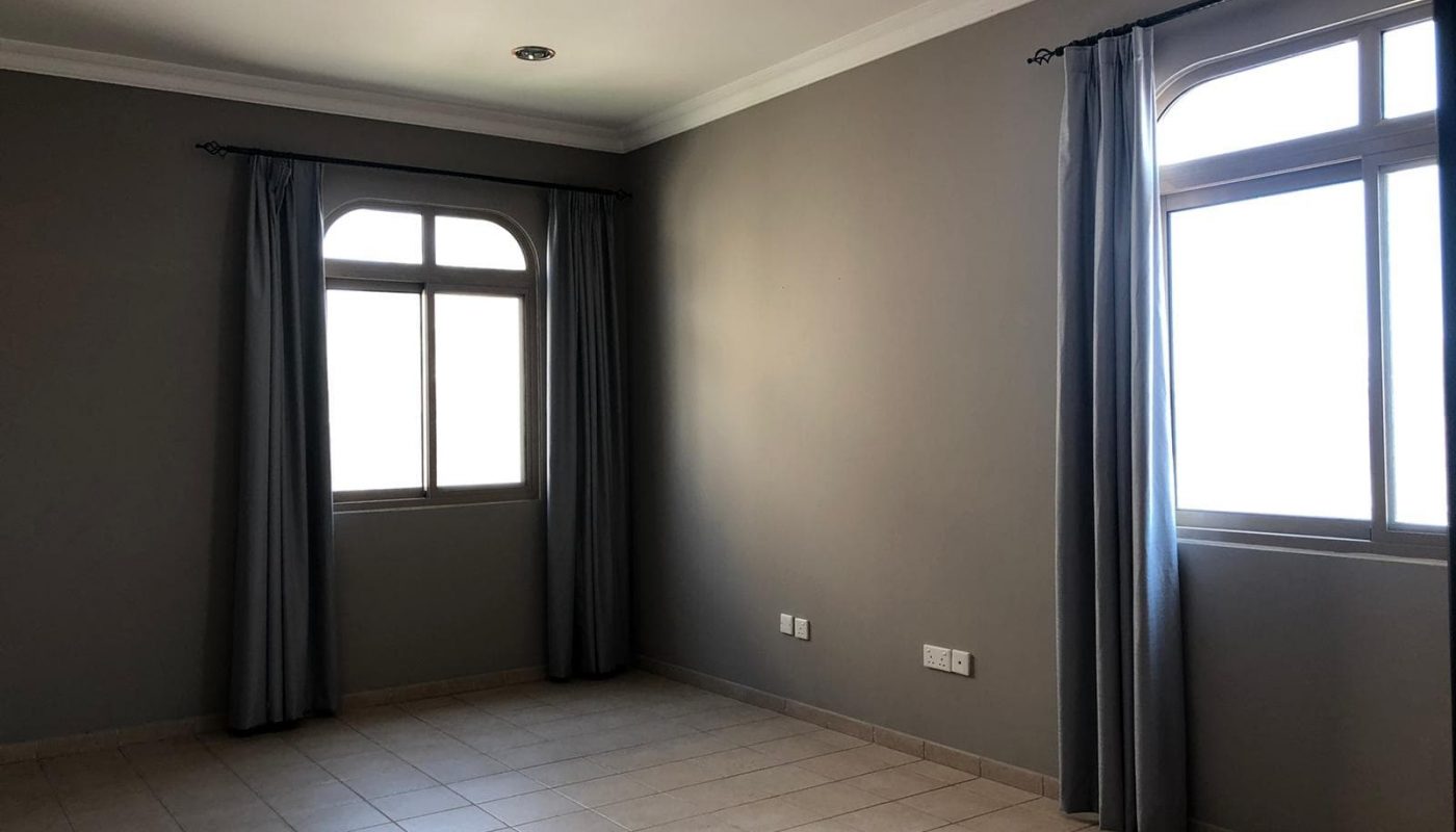 Empty room with gray walls, tile flooring, two windows with gray curtains, and ceiling lights.