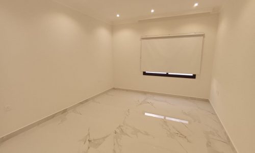 A spacious room with a white floor and a window.