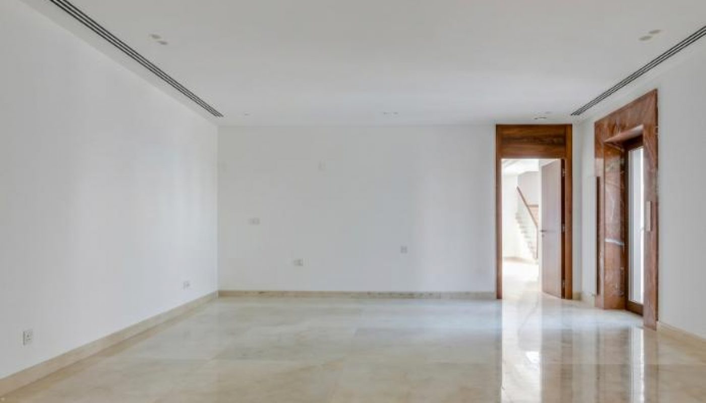Empty room with white walls, a polished beige marble floor, and wooden door frames leading to adjacent spaces.