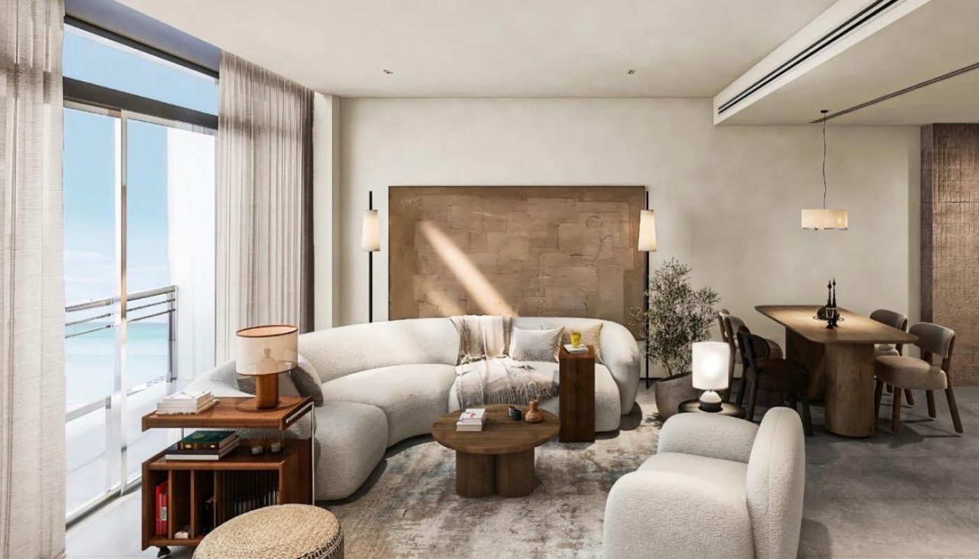 Modern living and dining area with curved sofa, neutral tones, large window with sheer curtains, wooden furniture, and contemporary decor. Ocean view visible through the window.