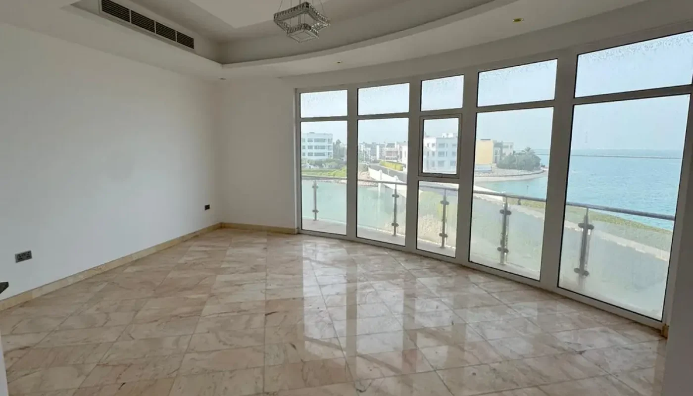 Empty room with marble floors, white walls, a modern ceiling design, large windows, and a view of buildings and water outside.