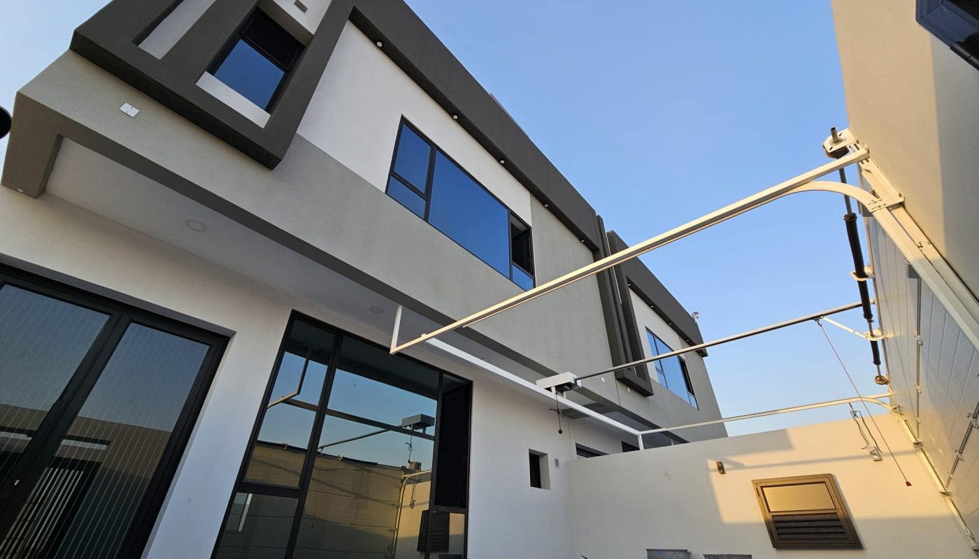 Modern two-story house with large windows and a minimalist design. The exterior is a combination of white and gray tones. A clothesline is installed in the backyard.