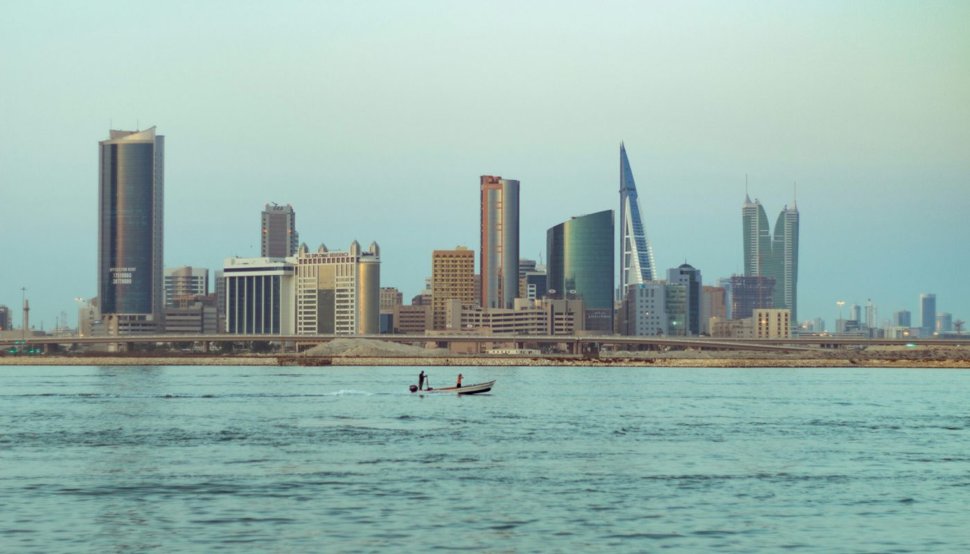 Two people in a small boat drift on calm water with Bahrain’s modern city skyline and high-rise buildings in the background, reflecting 2026 real estate trends.