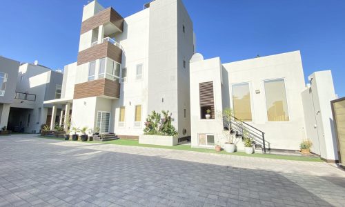 A large white house nestled in Al Janabiyah, featuring a brick walkway leading up to its entrance.