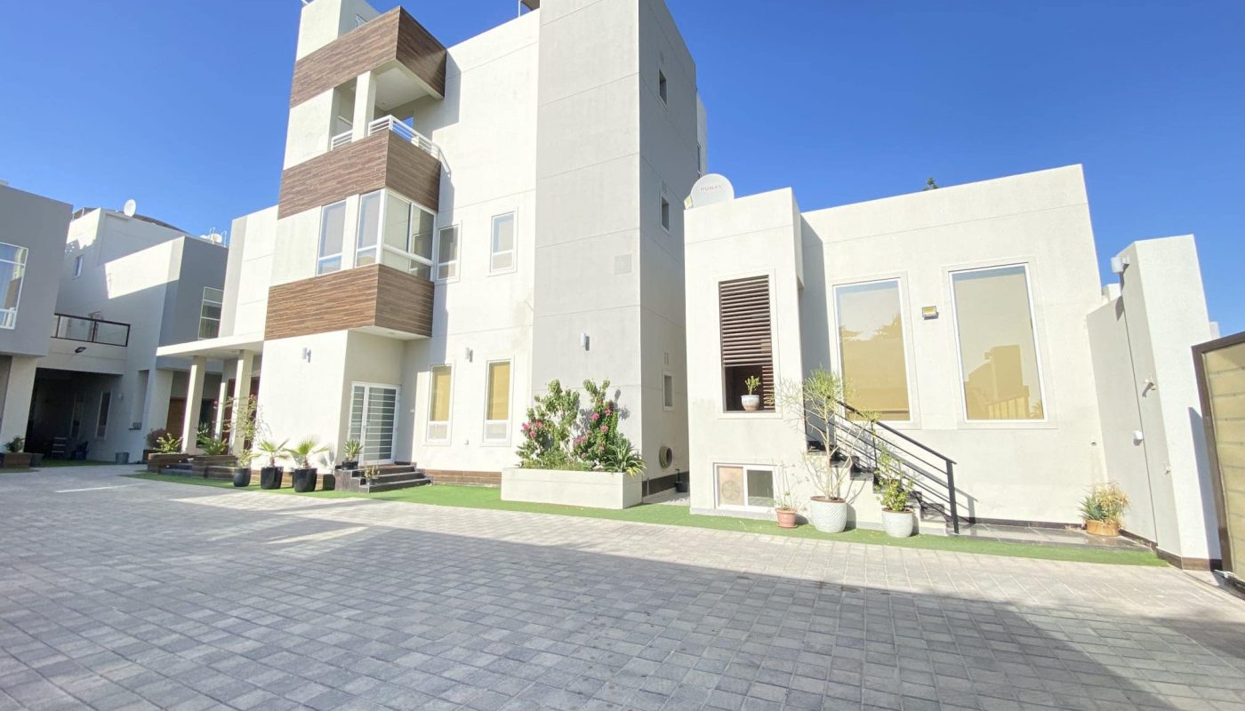 A large white house nestled in Al Janabiyah, featuring a brick walkway leading up to its entrance.