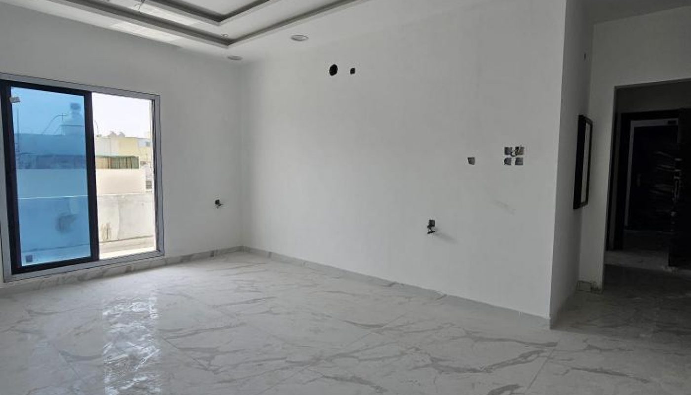 Empty, unfurnished room with white walls, large floor tiles, a recessed ceiling, and a sliding glass door leading to a balcony; visible electrical outlets and wiring.