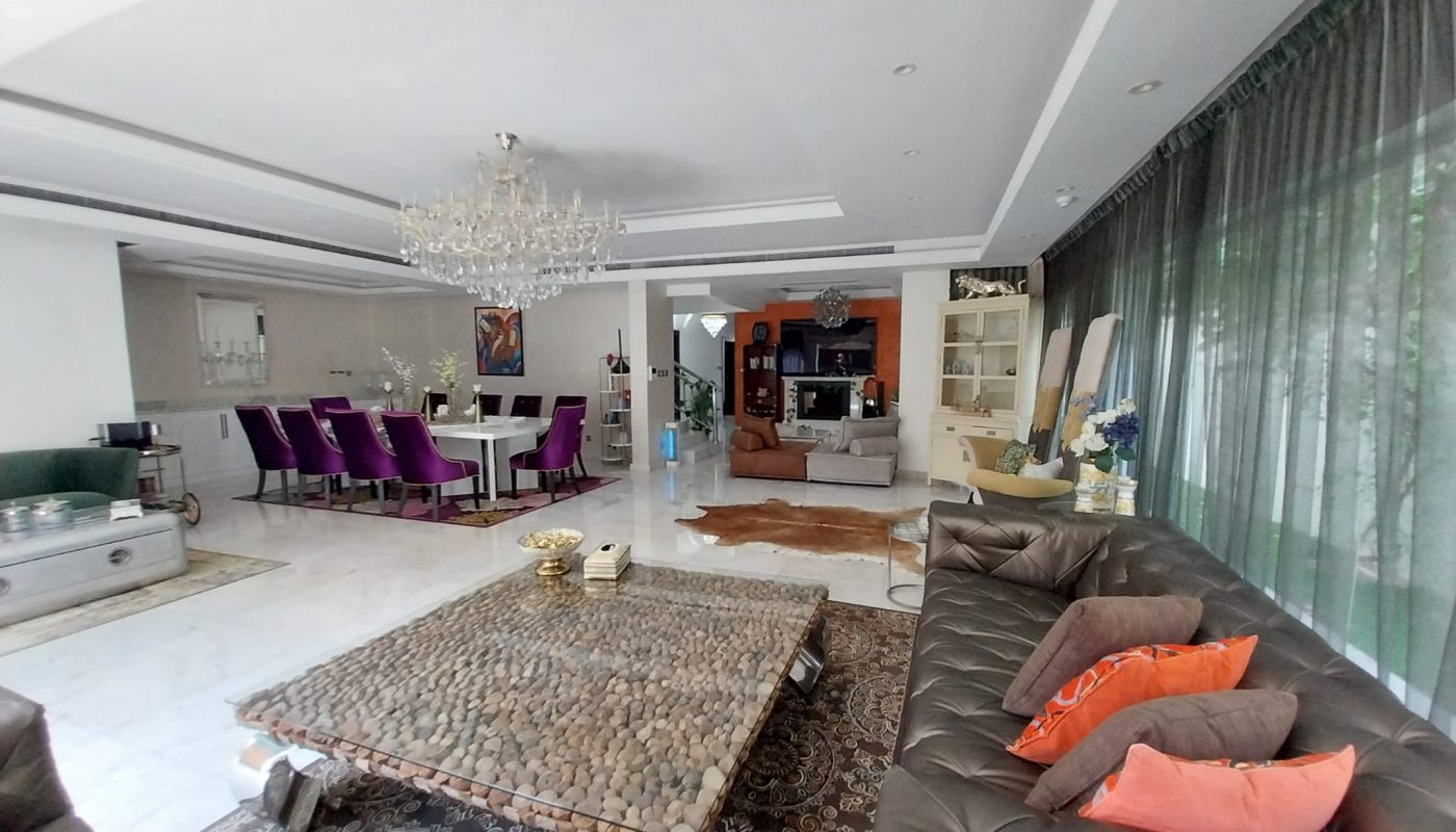 Spacious living and dining area with modern furniture, glass coffee table, chandeliers, purple dining chairs, and large windows with sheer curtains.