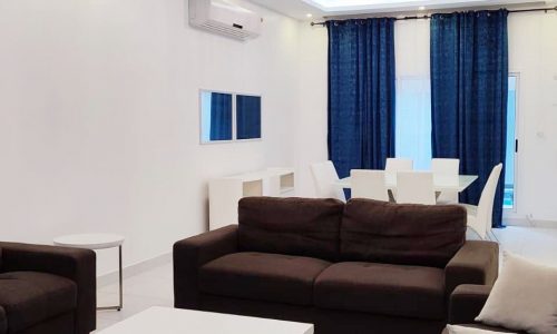 Modern living room interior in a fully furnished villa for rent with white walls, a brown sofa set, and blue curtains in Arad.