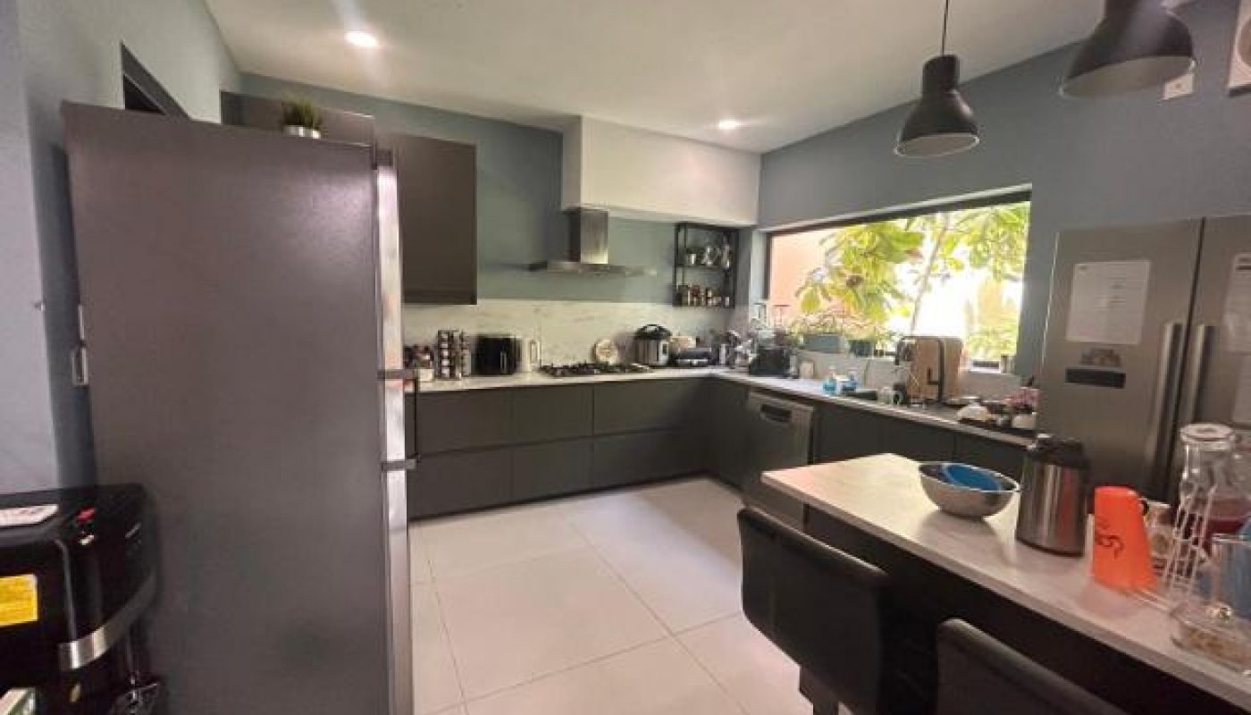 A modern kitchen with dark gray cabinets, a stainless steel refrigerator, and a large window overlooking greenery.