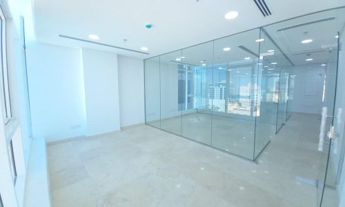 An empty, bright office with glass walls and windows in a new building located in the heart of Seef.