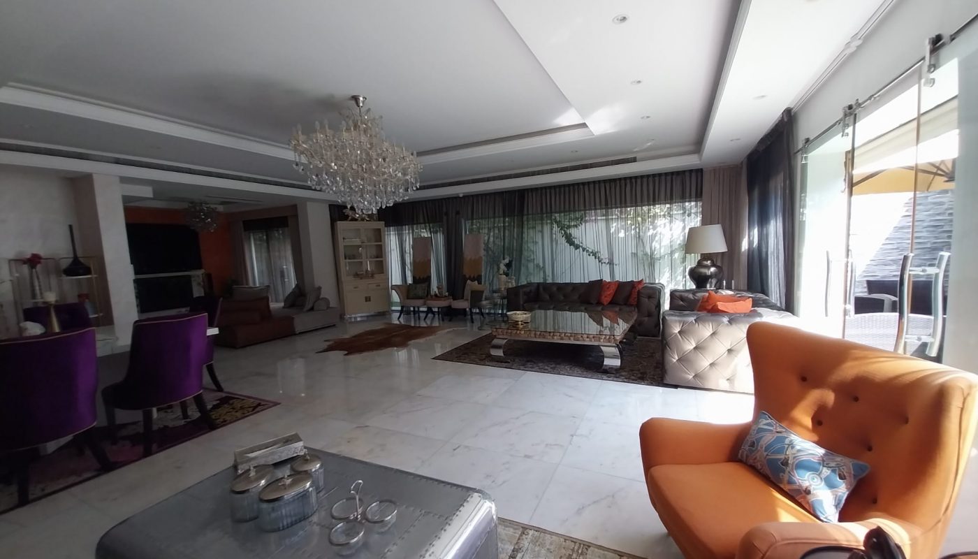 Spacious modern living room with large windows, a chandelier, assorted seating including an orange armchair, and a metal coffee table on a tiled floor.