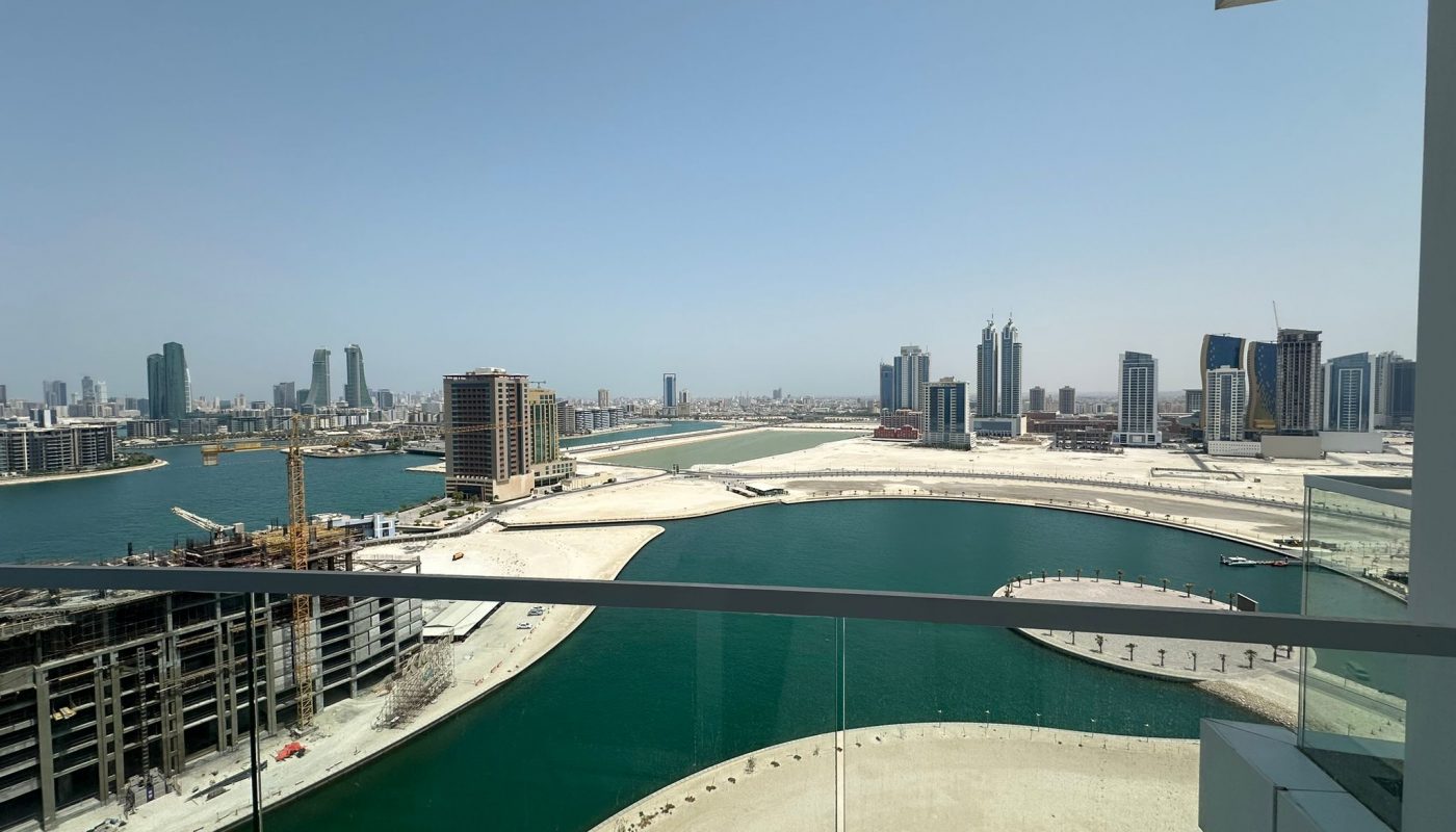 View from a balcony overlooking a curved waterway and construction sites, with tall buildings and a clear sky in the background.