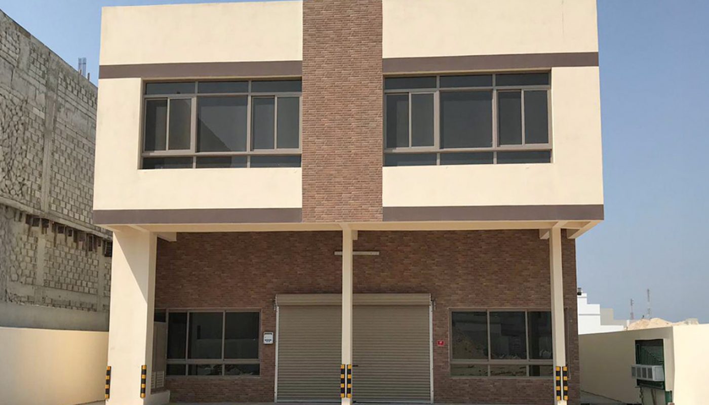 A two-story commercial building with a flat roof, large windows, and a brick façade, situated on a paved lot under a clear blue sky.