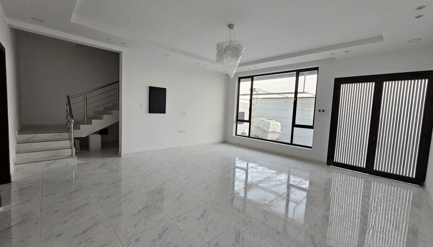 Spacious, modern living room with white marble floor, large windows, a glass door, a staircase on the left, and a chandelier.