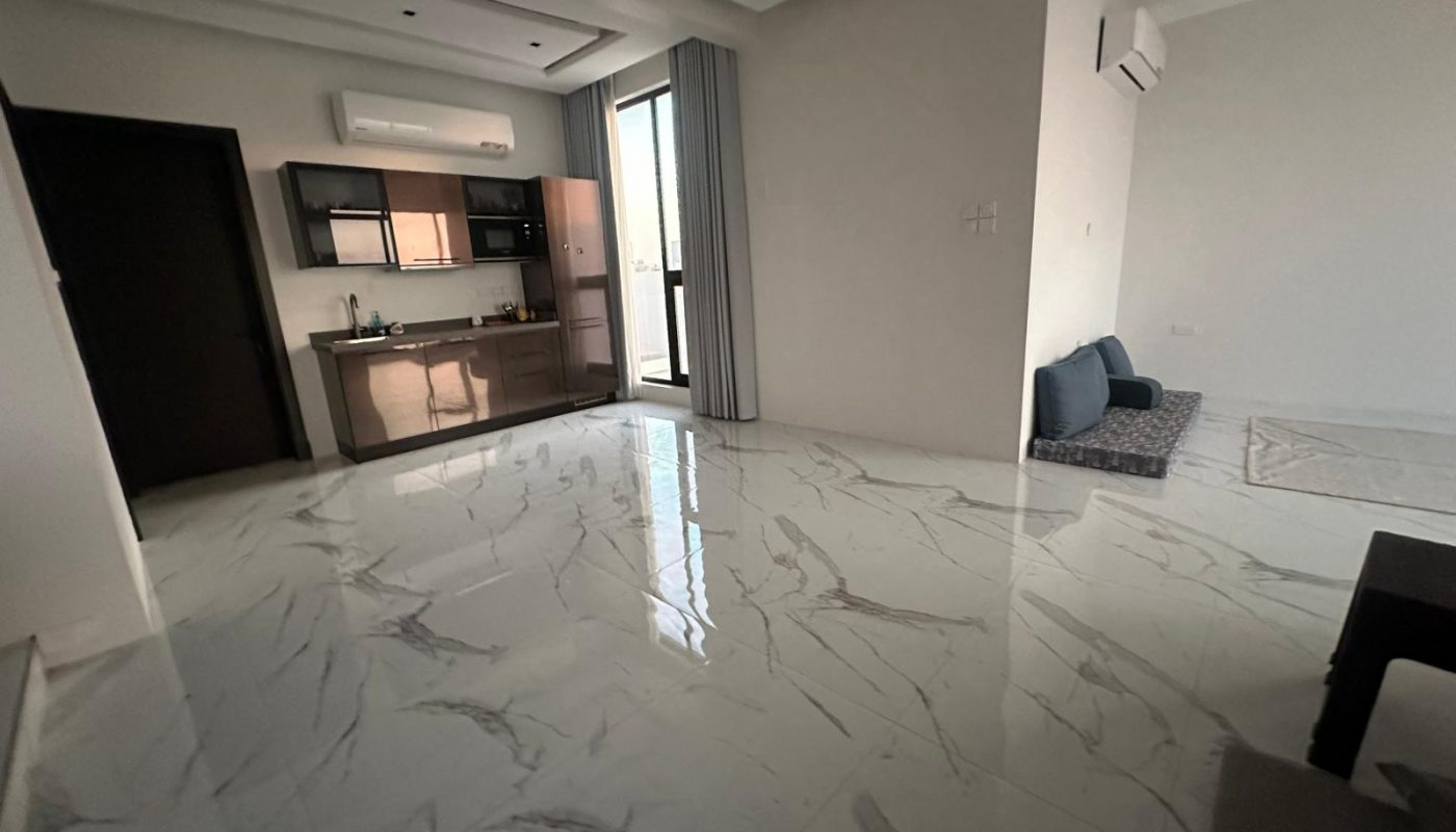 A modern room with a marble floor, small kitchen area, wall-mounted air conditioner, and a seating area with cushions and a low table near the wall.