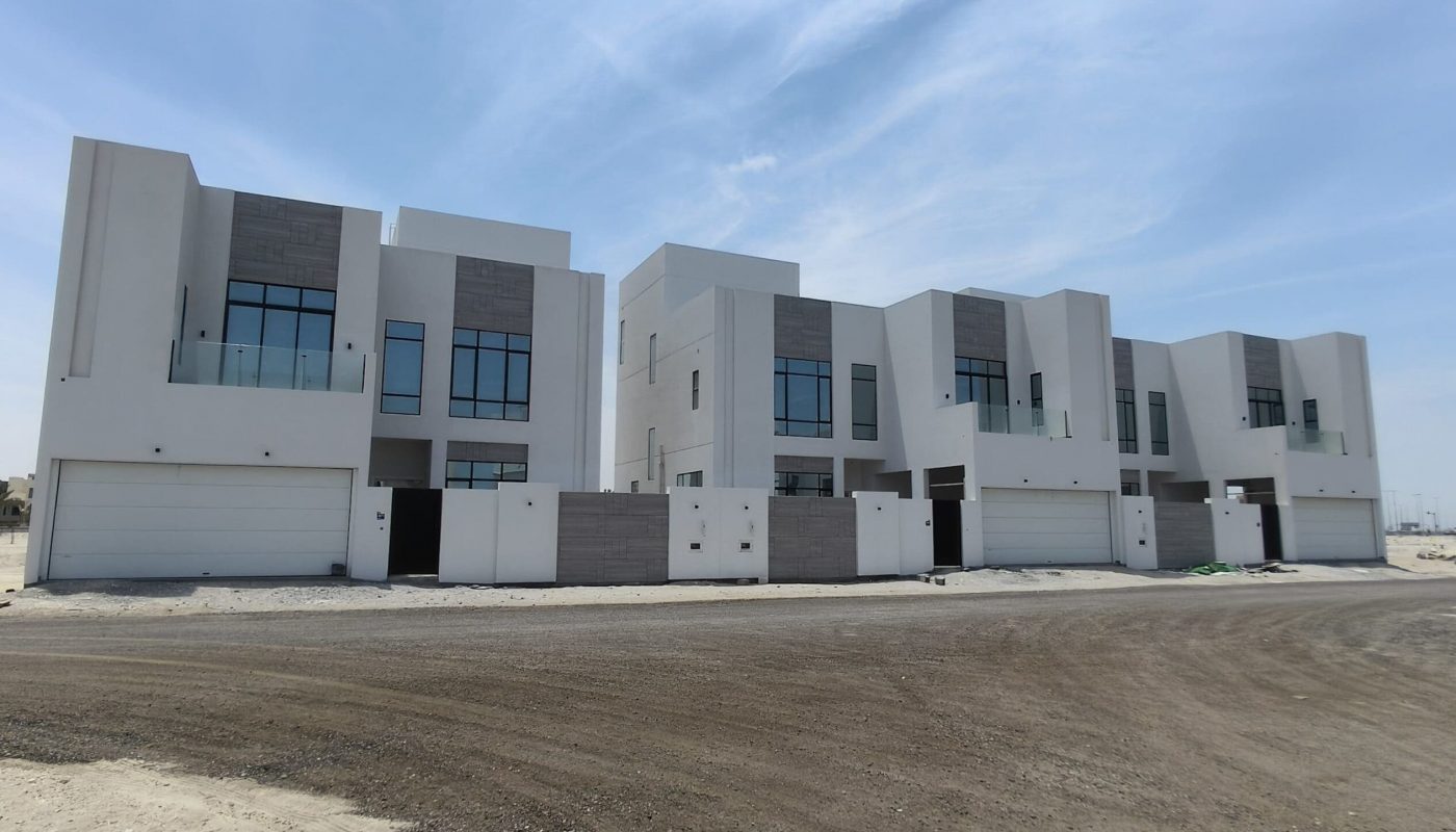 A row of modern, white two-story houses with large windows and attached garages under a partly cloudy sky.