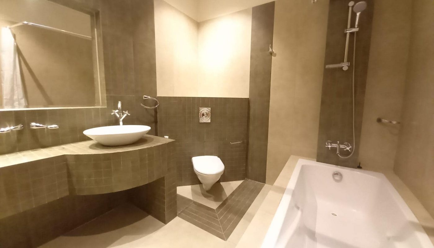 A modern bathroom with a bathtub, wall-mounted toilet, floating sink, large mirror, and tiled walls.