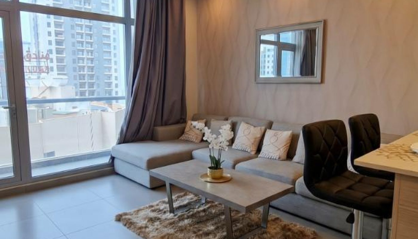 Modern living room with a sectional sofa, throw pillows, coffee table, rug, bar stools, large windows, and city view.
