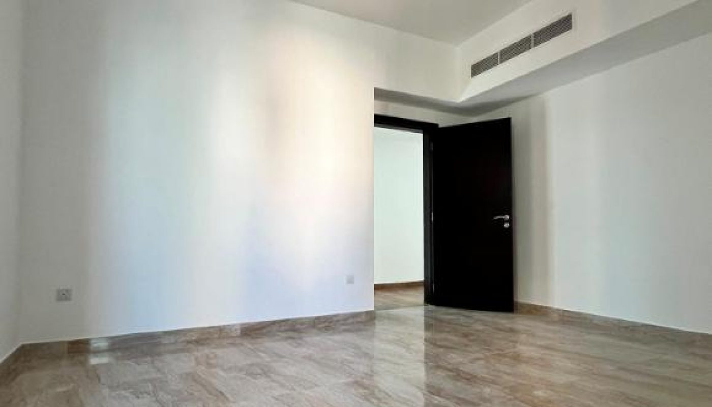 Empty room with beige marble floor, white walls, ceiling light, and an open dark door. Air vents are visible above the doorway on the right wall.