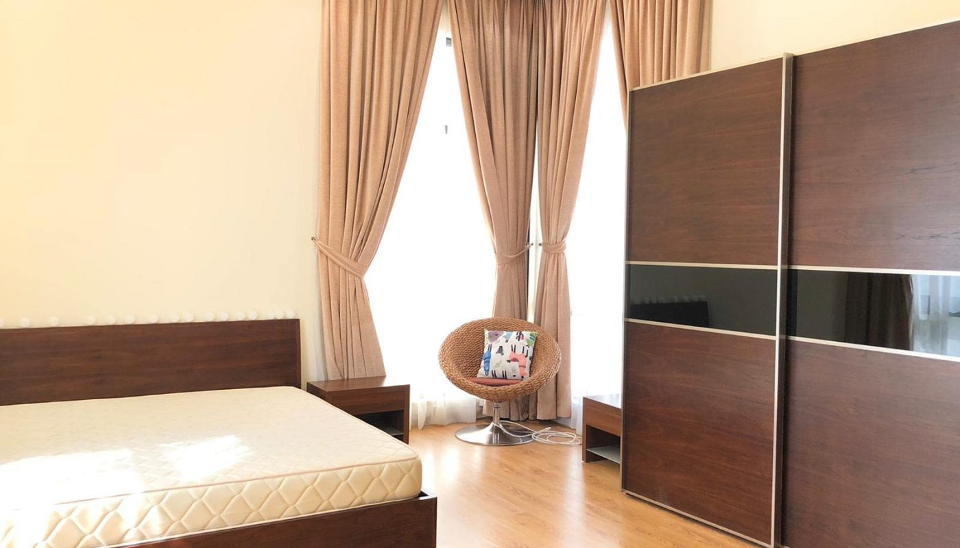 A spacious bedroom features a bed with a bare mattress, a large wardrobe with sliding doors, a chair with a decorative pillow, and large curtained windows allowing ample natural light to enter.