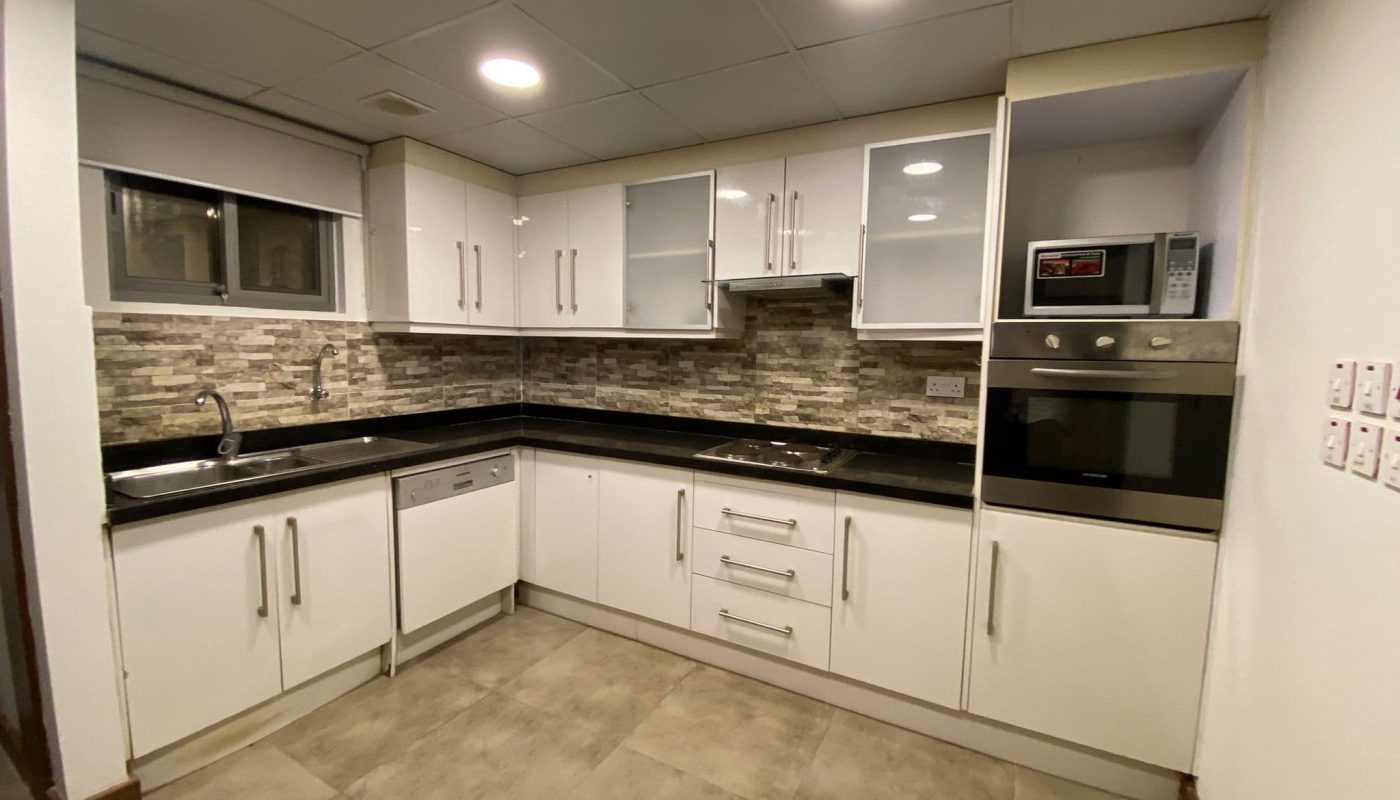 Modern kitchen with white cabinets, built-in oven, microwave, dishwasher, black countertop, sink, and tiled backsplash.
