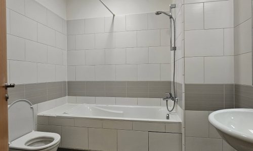 A flat for rent featuring a bathroom with a white toilet, a bathtub with a showerhead, and a white sink, all set against tiled walls and a tiled floor. Perfectly situated near the serene Reef Island.