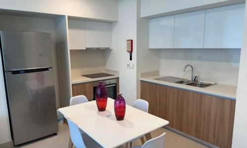 Luxurious modern kitchen with white cabinets, wooden countertops, a sink, a white table with chairs, and two pink vases, complemented by a stainless steel fridge.