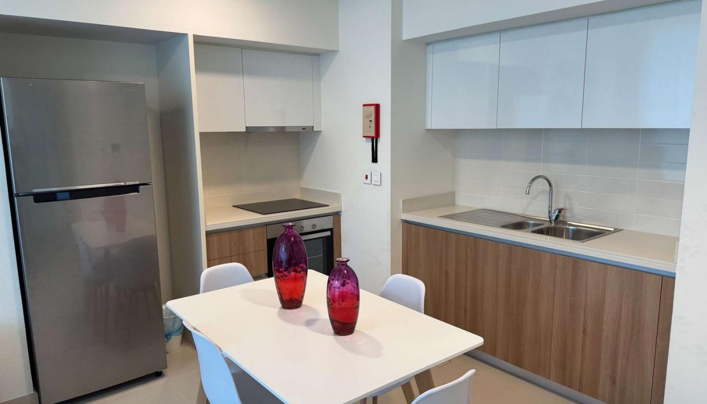 Modern kitchen with a stainless steel fridge, built-in oven, white cabinets, dining table with four chairs, and two red vases on the table.