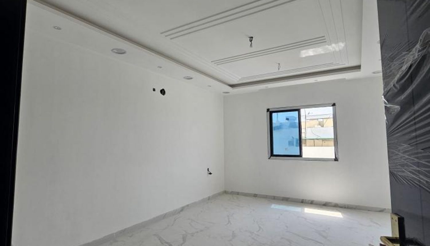 Empty, unfurnished white room with marble-patterned tile floor, a window letting in natural light, and unfinished ceiling fixtures.