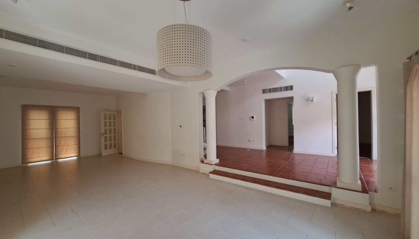Spacious empty room with tiled floor, white walls, large ceiling light, arched entryway, and windows with beige blinds.