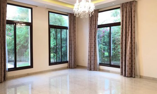 A luxurious Al Jasra villa available for rent, featuring a large empty room with large windows and a captivating chandelier.