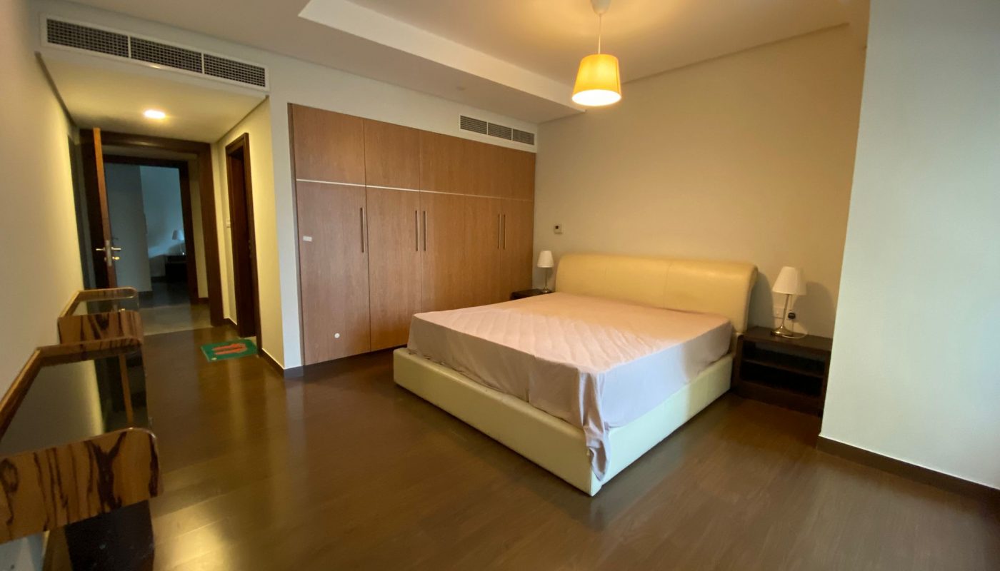 A modern bedroom with a double bed, wooden floor, built-in wooden wardrobes, two bedside tables with lamps, and a ceiling light.