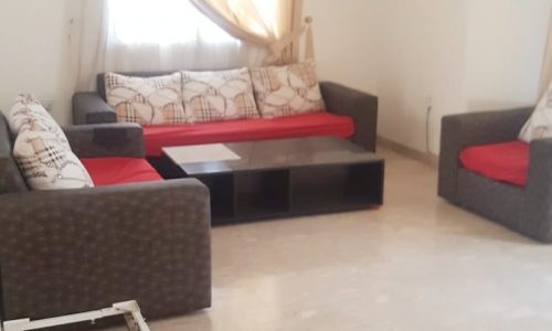 A villa in Busaiteen available for rent, featuring a living room with red couches and a television.