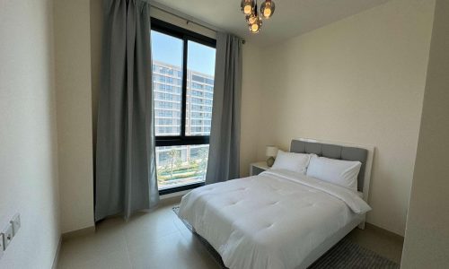 A modern 2 bedroom apartment with a single white bed, gray curtains, and a view of urban buildings from the window.