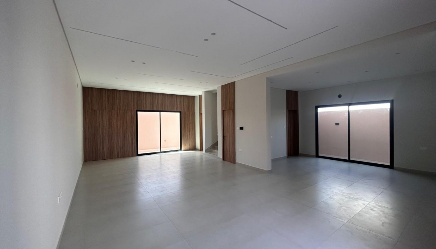 Spacious empty room with large tiled floor, white walls, wood panel accents, and two large sliding glass doors leading outside.
