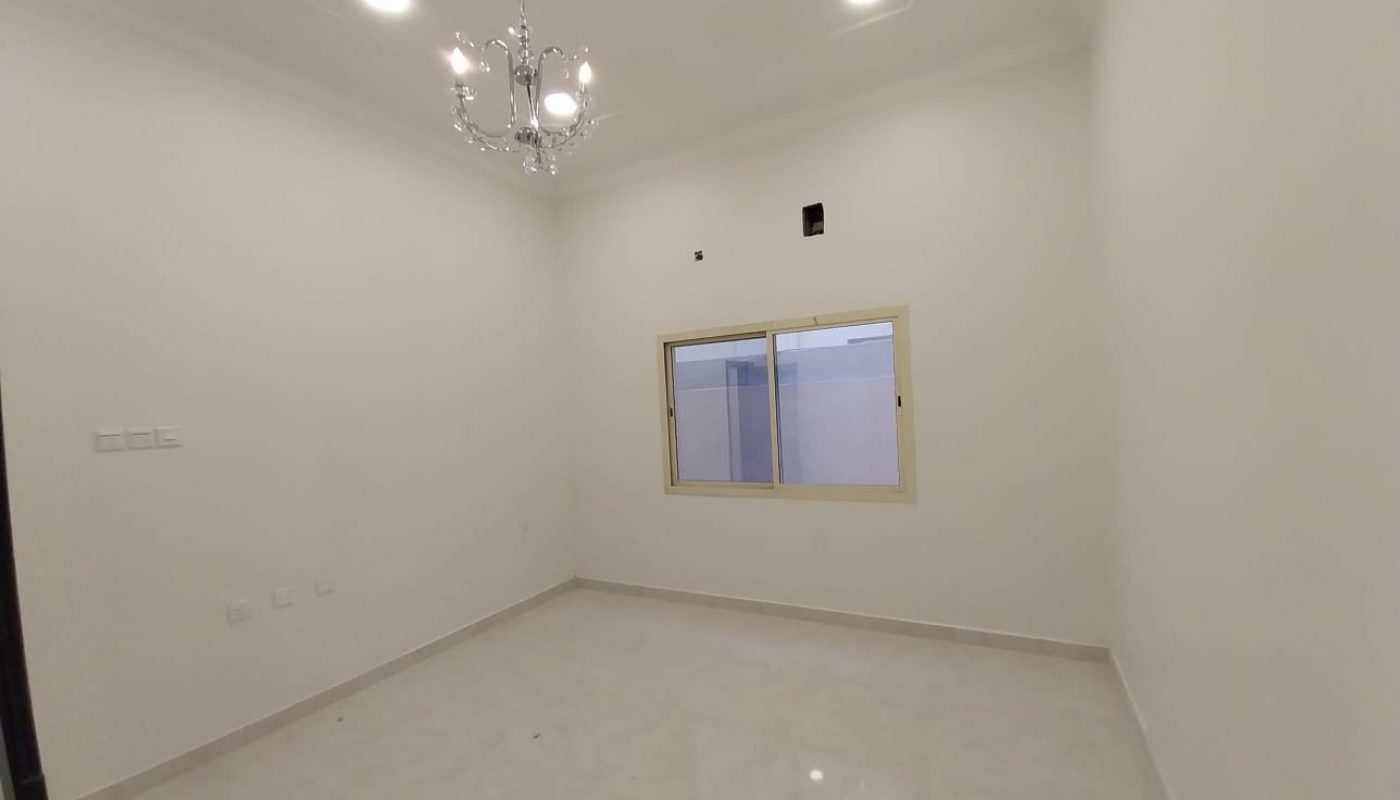 Empty, unfurnished room with white walls, tiled floor, a window, ceiling lights, and a small chandelier.