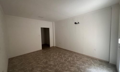 Empty room for rent in Al Hidd with beige floor tiles, white walls, and a small black security camera on the upper right wall.